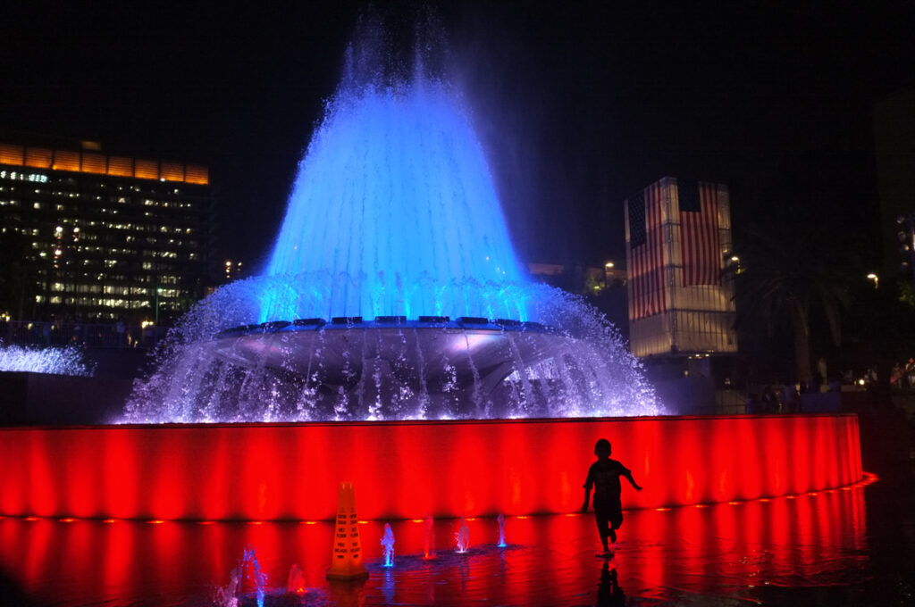 Silhouette of a boy running near a large fountain at Grand Park in Los Angeles, CA